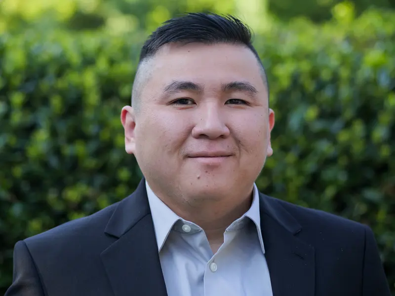 Second corporate headshot of a man in a suit with greenery behind him