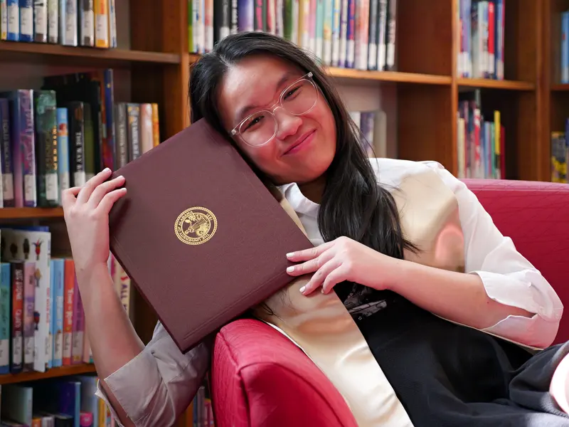Graduation portrait of a graduate holding a diploma in a library