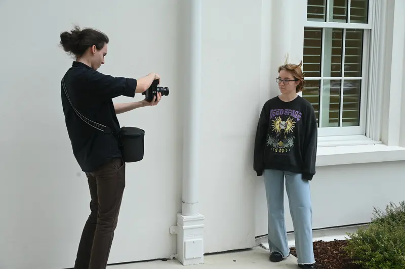 Camera operator filming a subject beside a white porch column