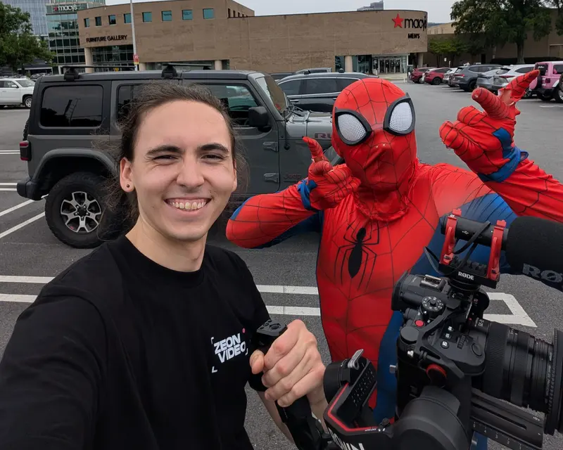 Director Dylan Baxter smiling next to a person in a Spider-Man costume in a parking lot