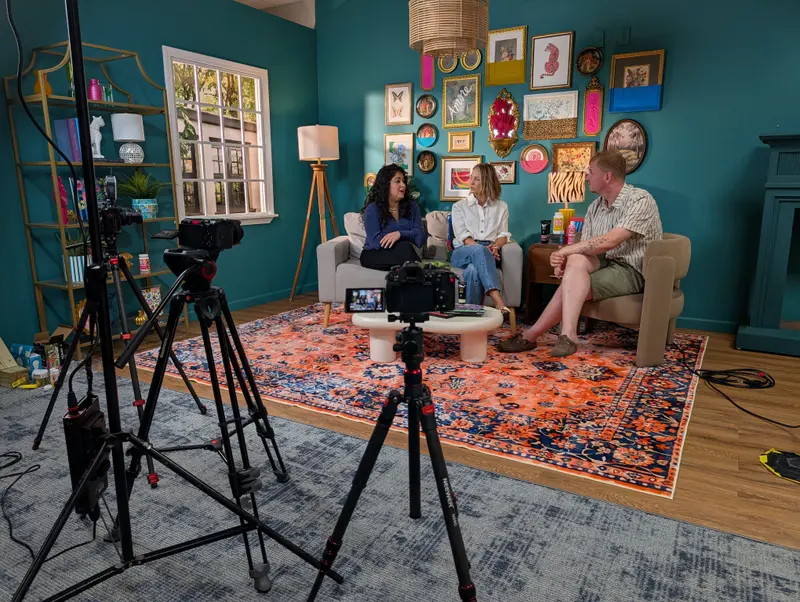 Three-person sit-down interview on a couch, lit and covered by cameras on tripods