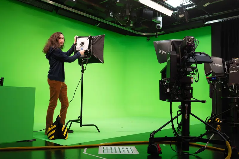 Crew member adjusting a softbox in a green-screen studio