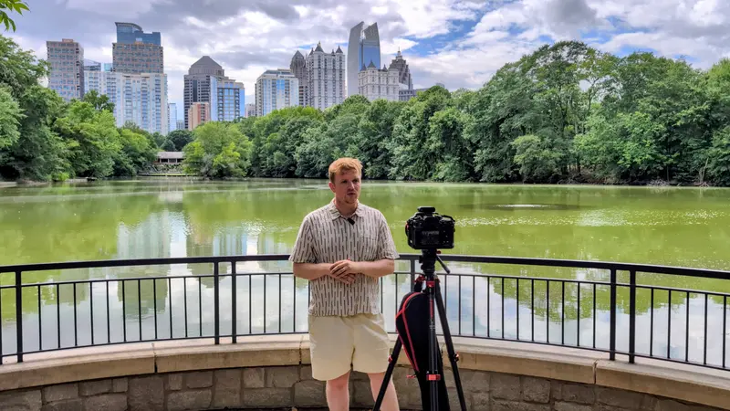 Presenter on camera at a lakeside overlook with the Atlanta skyline behind